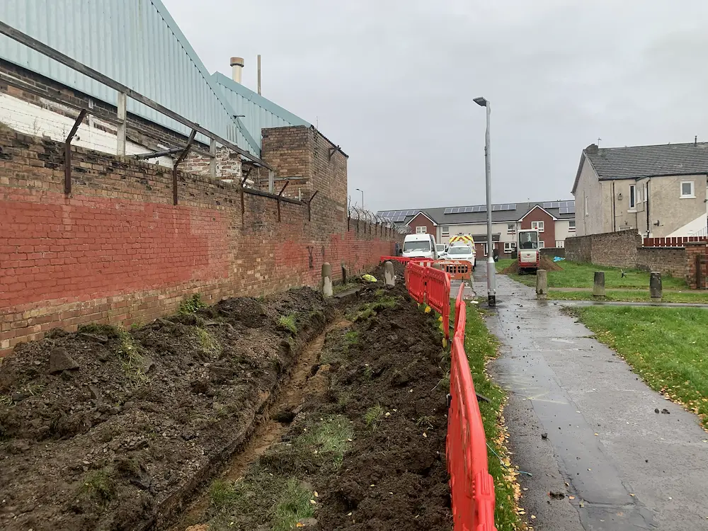 Backfilled cable trench along a boundary wall during a site electrical supply upgrade